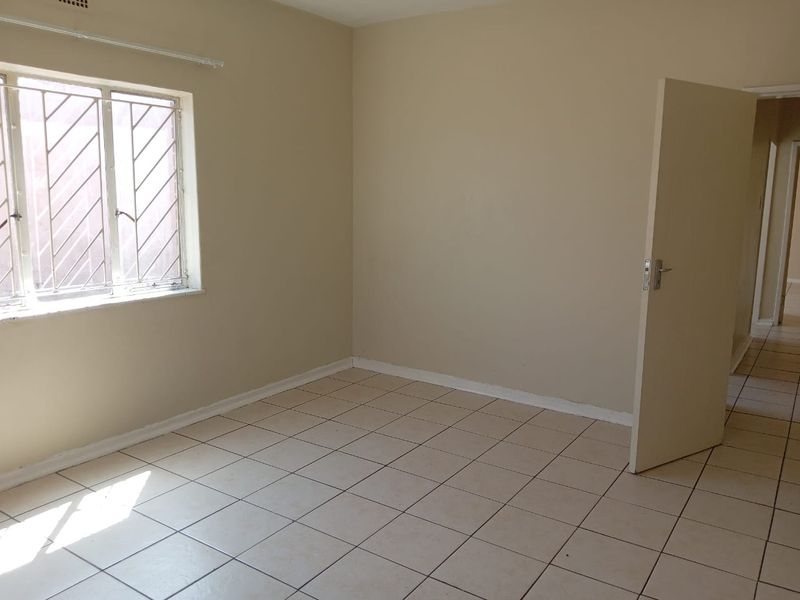 An empty bedroom featuring neutral wall paint, tiled flooring, and a window fitted with security bars.