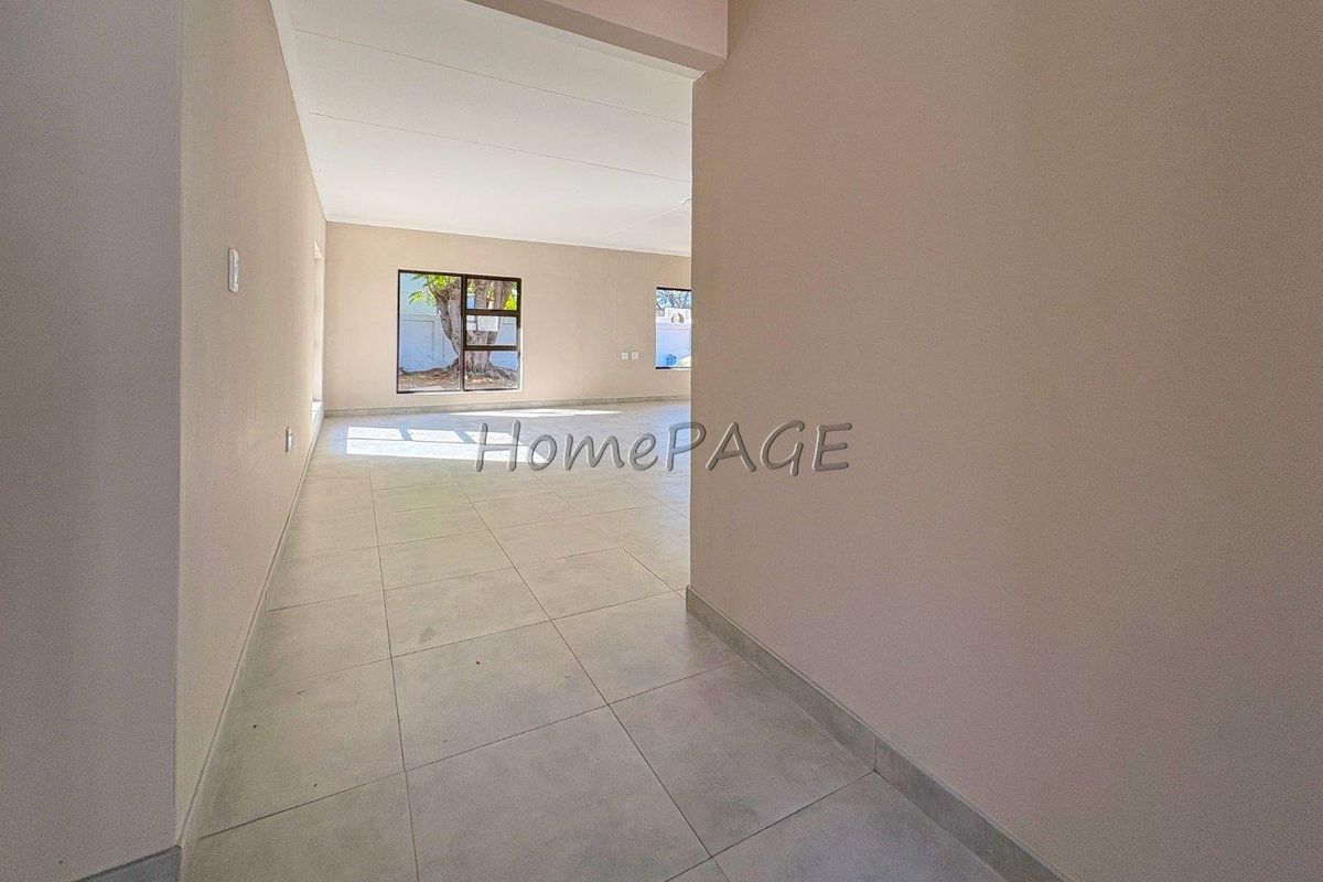 A spacious, empty living area featuring neutral tiled flooring and large aluminium-framed windows, offering a bright and versatile blank canvas.