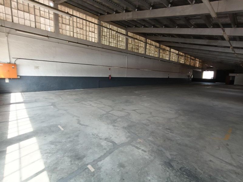 Spacious industrial warehouse area featuring high ceilings with exposed steel trusses, clerestory windows for natural light, and durable concrete flooring.