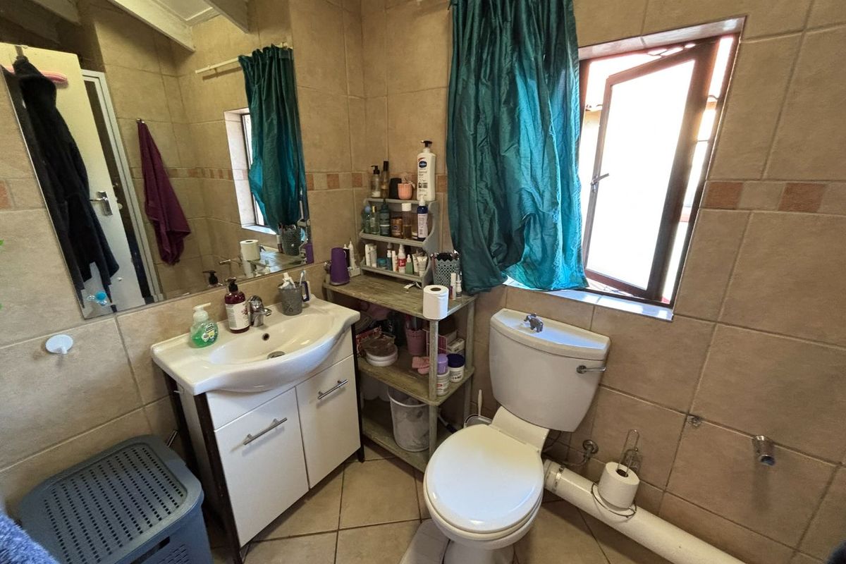 A functional bathroom featuring tiled walls and flooring, a vanity cabinet with basin, and a toilet. The space includes an exposed plumbing pipe.