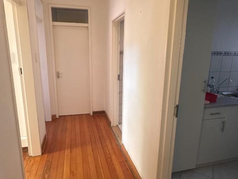 A bright hallway featuring polished hardwood flooring, recessed lighting, and access to multiple rooms, including a view into an adjacent kitchen area.