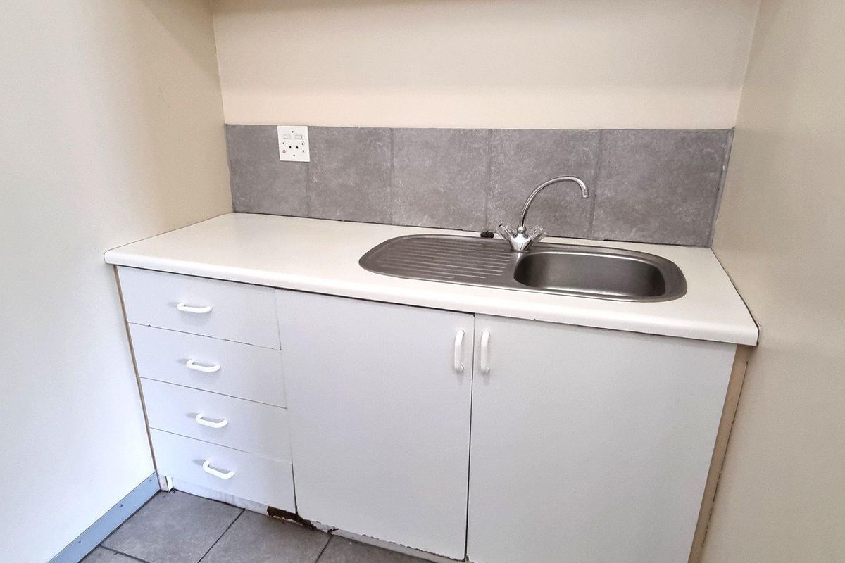 A functional kitchenette area featuring a stainless steel sink, white cabinetry, and grey tiled splashback, suitable for office utility use.