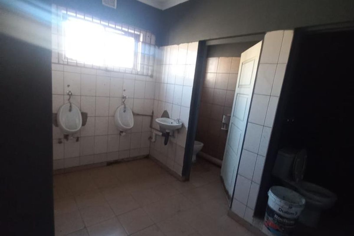 Industrial style communal bathroom facility featuring multiple urinals, a wall-mounted washbasin, and a separate toilet cubicle with tiled finishes.