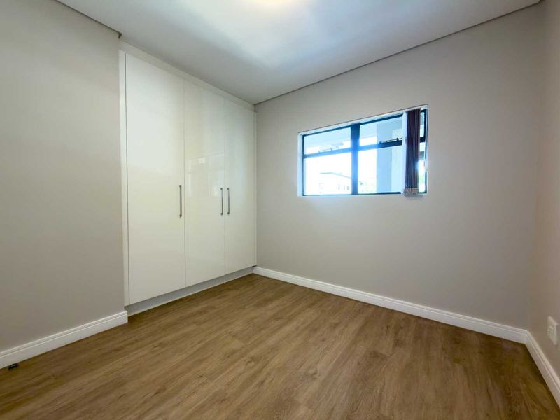 A clean, modern bedroom featuring neutral walls, light wood-look laminate flooring, and sleek white built-in cupboards.