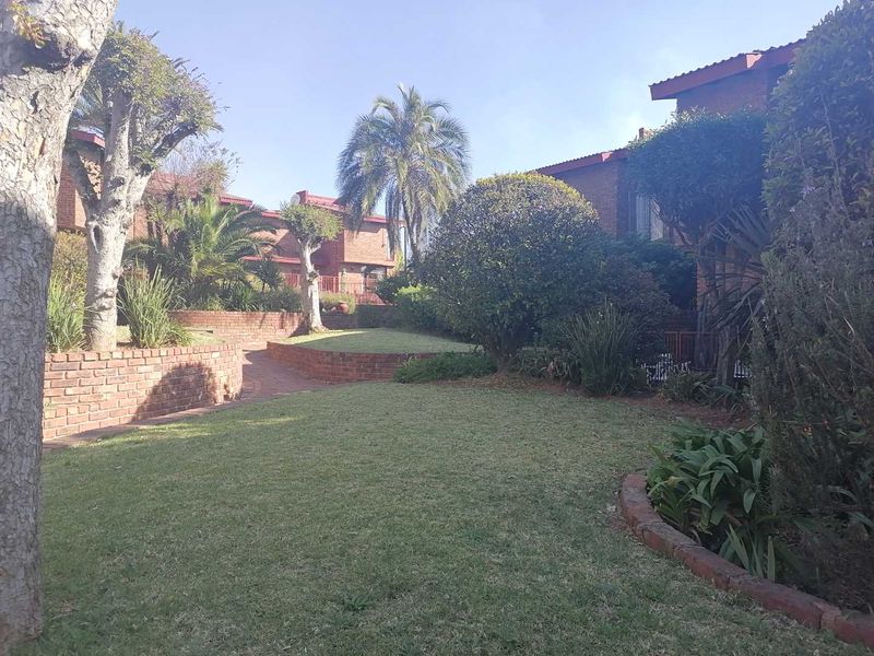 A well-maintained communal garden area featuring brick retaining walls, established landscaping, and paved pathways between townhouse units.