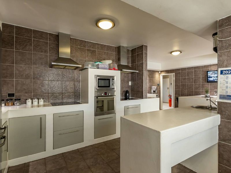A functional kitchen featuring built-in appliances, tiled splashbacks, a central island with a sink, and ample cabinetry for storage.