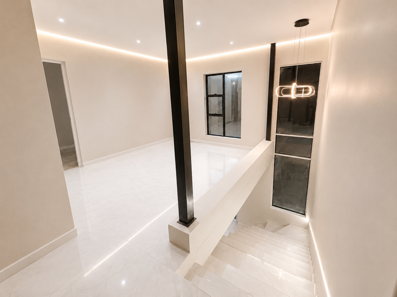 A modern, minimalist landing area featuring polished porcelain tiles, recessed cove lighting, a striking black support column, and a contemporary staircase with integrated lighting.