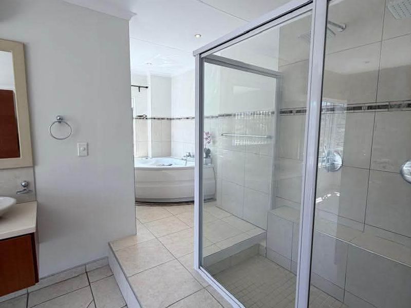 Spacious bathroom featuring a raised platform with a glass-enclosed shower, built-in shower bench, and a corner bathtub with neutral tile finishes.