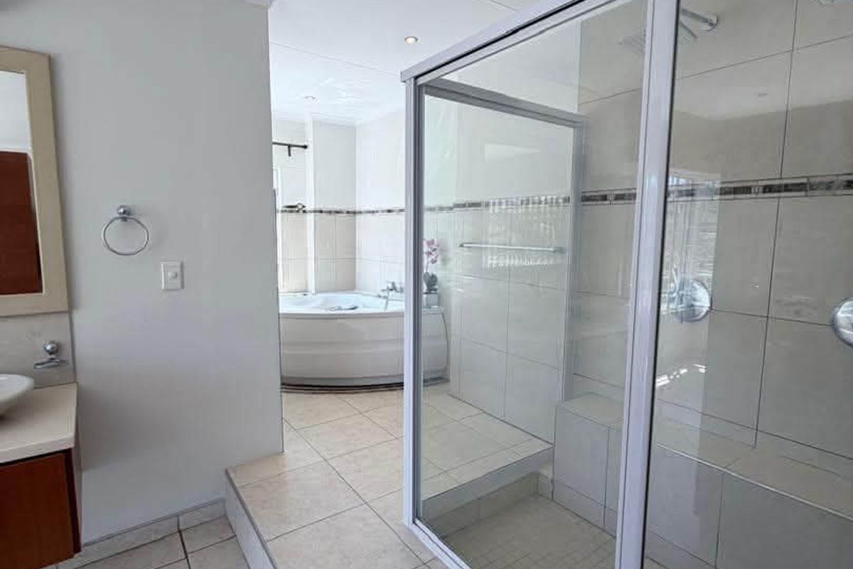 Spacious bathroom featuring a raised platform with a glass-enclosed shower, built-in shower bench, and a corner bathtub with neutral tile finishes.