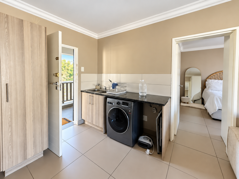 A functional laundry area featuring built-in cabinetry, a granite countertop with an integrated sink, and tiled flooring, conveniently located near the apartment entrance.