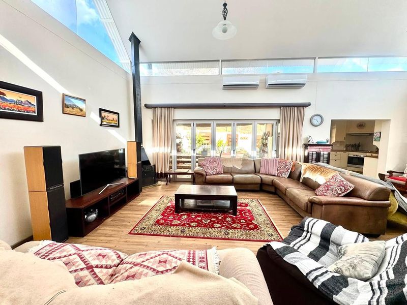 Spacious open-plan living area featuring a vaulted ceiling, clerestory windows for natural light, a wood-burning fireplace, and bi-fold doors leading to the outdoors.