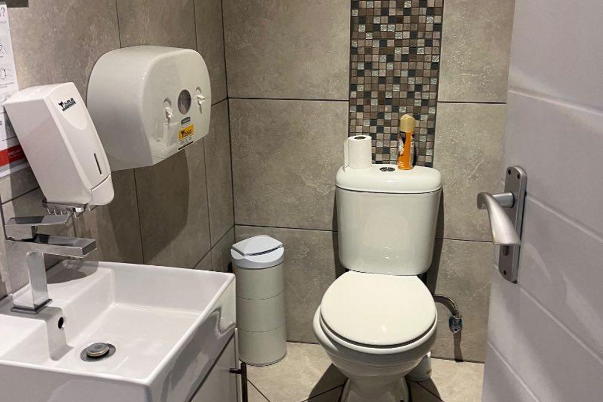 A compact commercial restroom featuring tiled walls with mosaic accents, a modern vanity basin, and a standard toilet suite.