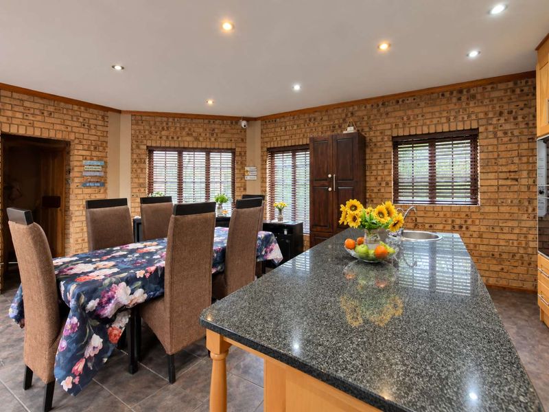Open-plan kitchen and dining area featuring exposed brick walls, a granite-topped island, and warm timber cabinetry with recessed lighting.