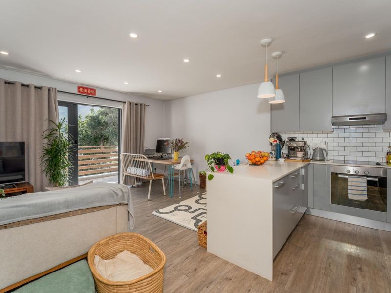Modern open-plan living area featuring a sleek kitchen with grey cabinetry, subway tile backsplash, and a functional island, flowing onto a private balcony.