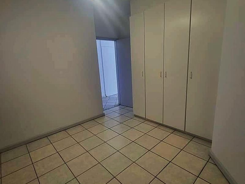 An empty bedroom featuring tiled flooring, built-in cupboards, and a ceiling fan, offering a clean and neutral space ready for personalization.