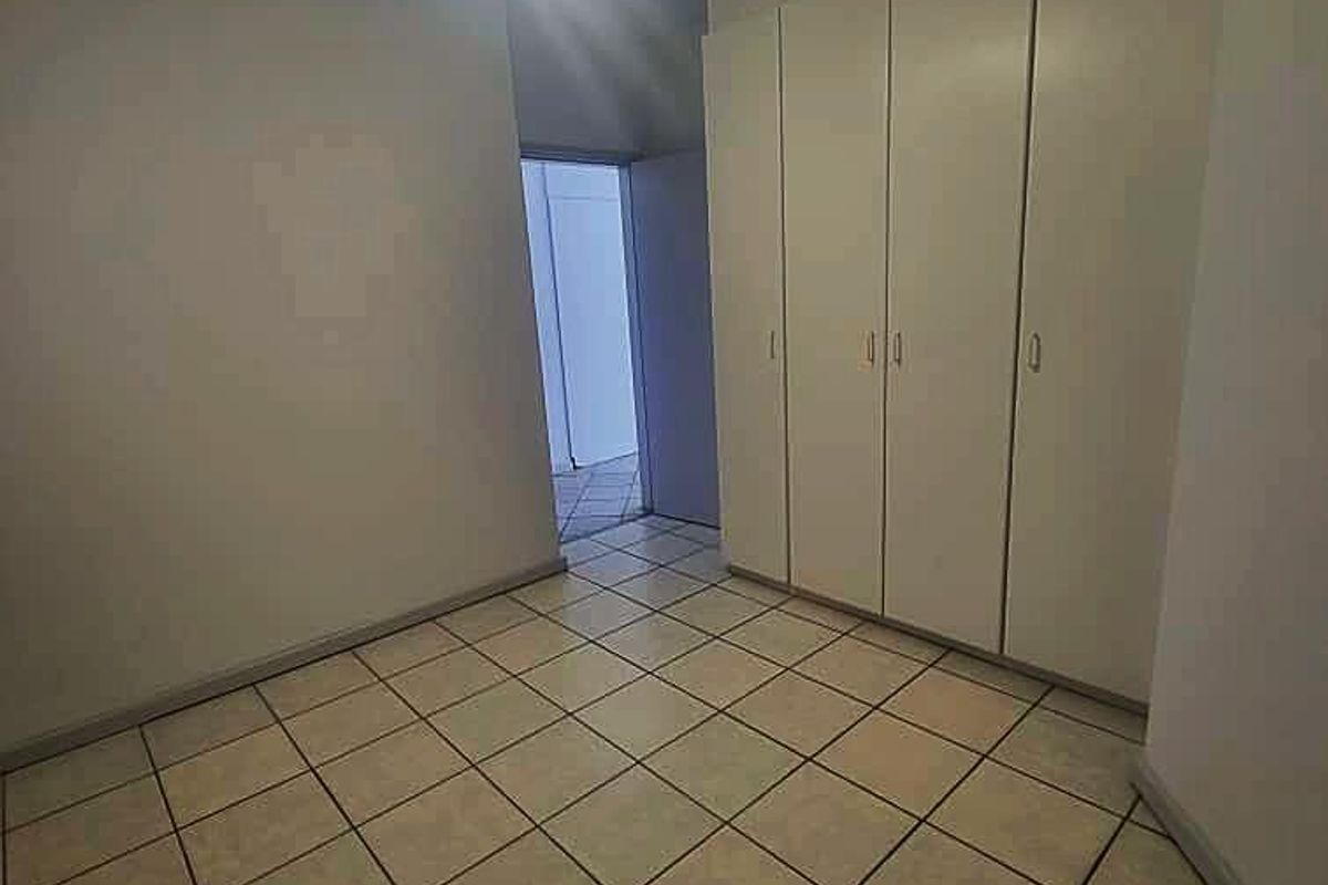 An empty bedroom featuring tiled flooring, built-in cupboards, and a ceiling fan, offering a clean and neutral space ready for personalization.