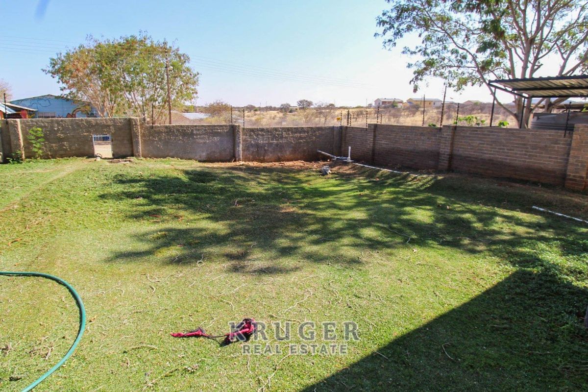 A spacious rear garden area featuring a brick perimeter wall with electric fencing and an open lawn space.