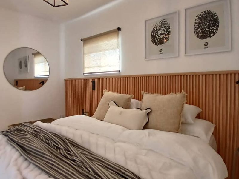 A well-appointed bedroom featuring a modern timber slat headboard, neutral decor, and a contemporary pendant light fixture.