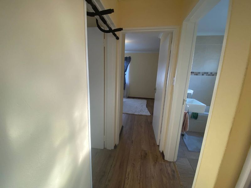 A functional hallway connecting the bedroom and bathroom, featuring laminate flooring and neutral wall finishes.