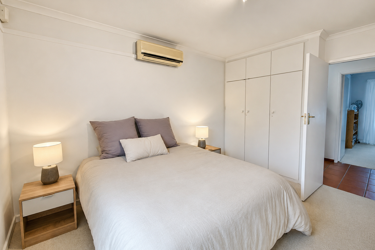 A well-maintained bedroom featuring neutral carpet, built-in wardrobes, and a wall-mounted split-system air conditioner.