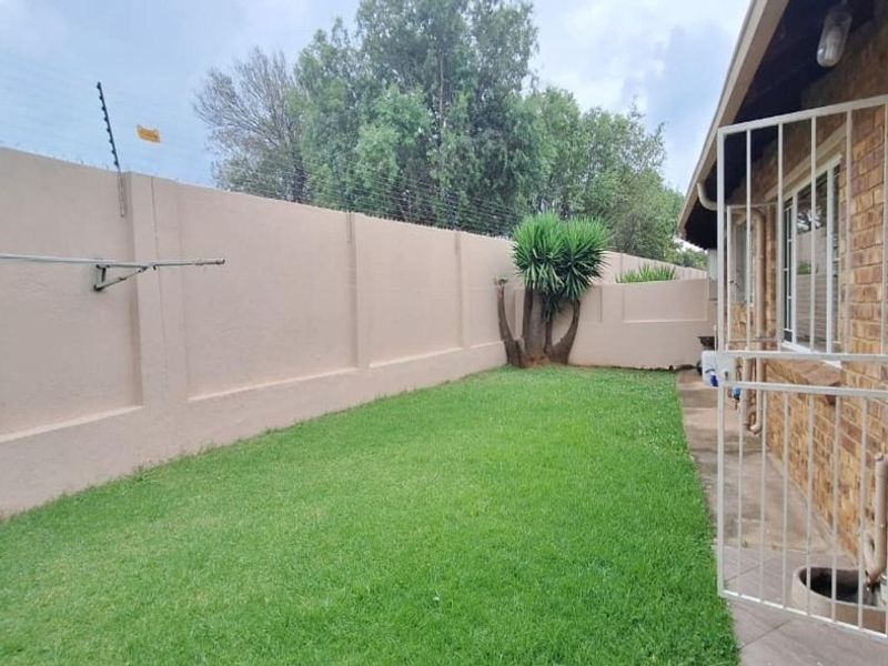 A private rear garden area featuring a well-maintained lawn, perimeter wall with electric fencing, and direct access to the townhouse via a security gate.