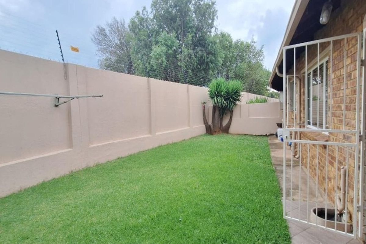 A private rear garden area featuring a well-maintained lawn, perimeter wall with electric fencing, and direct access to the townhouse via a security gate.