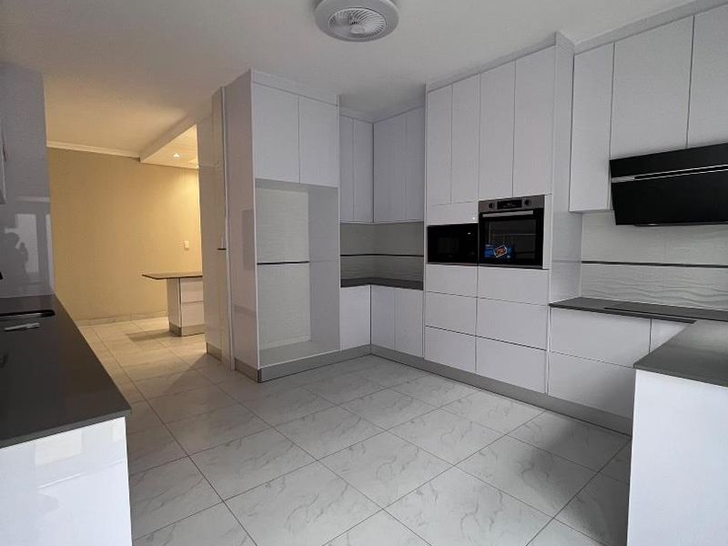 Modern kitchen featuring sleek white cabinetry, integrated appliances, stone countertops, and large format marble-look floor tiles.