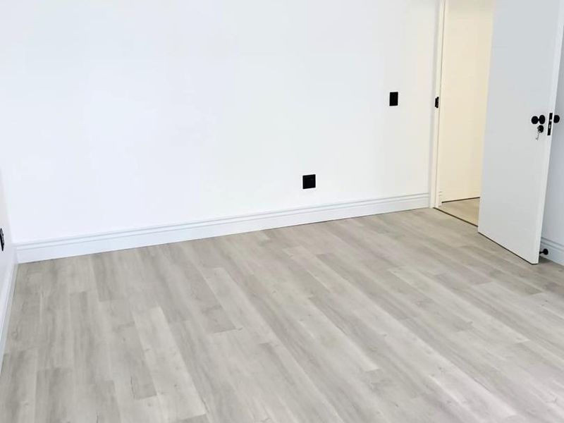 A bright, empty bedroom featuring modern light-toned laminate flooring, crisp white walls, and a clean, minimalist aesthetic.