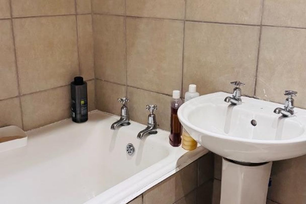 A functional bathroom featuring a standard bathtub and a pedestal basin with tiled walls and flooring.