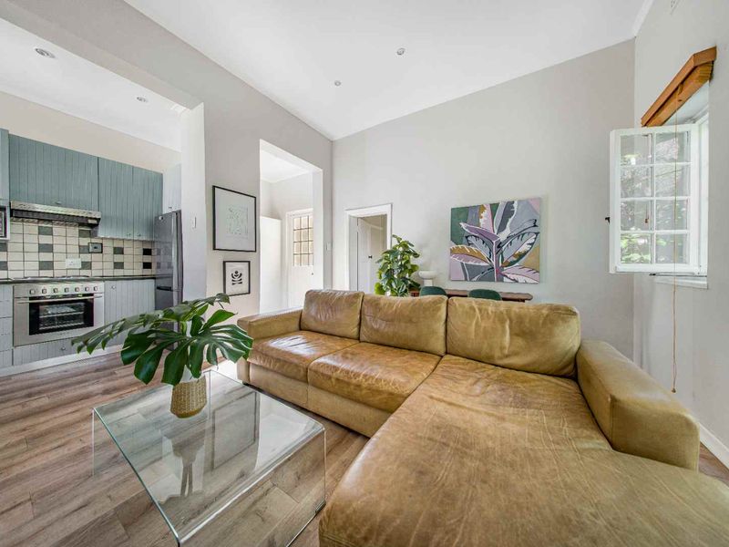 Open-plan living area featuring a modern kitchen with built-in appliances, tiled backsplash, and laminate flooring, seamlessly flowing into a comfortable lounge space.