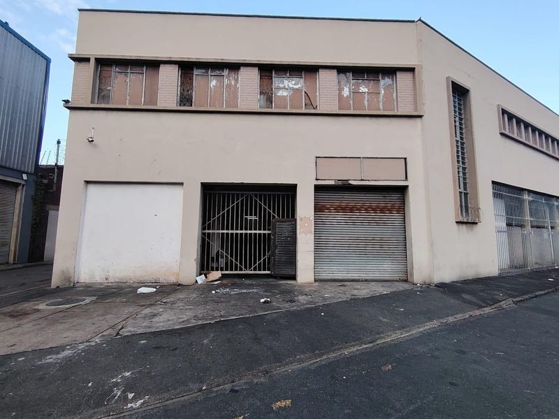 Industrial building facade featuring a roller shutter door, security gate, and multi-pane windows, showing signs of wear and requiring maintenance.