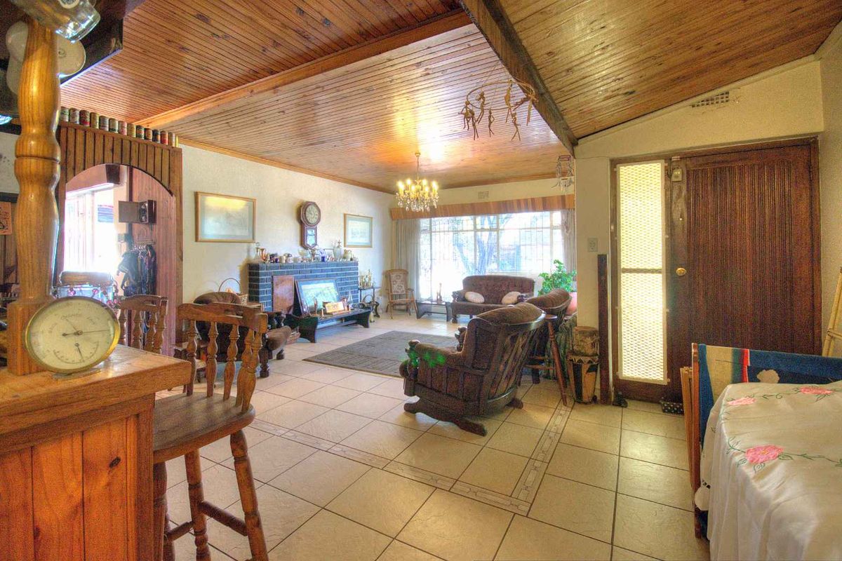 Spacious living area featuring a timber-clad ceiling, tiled flooring, and a brick fireplace, offering a traditional layout with direct access to the exterior.