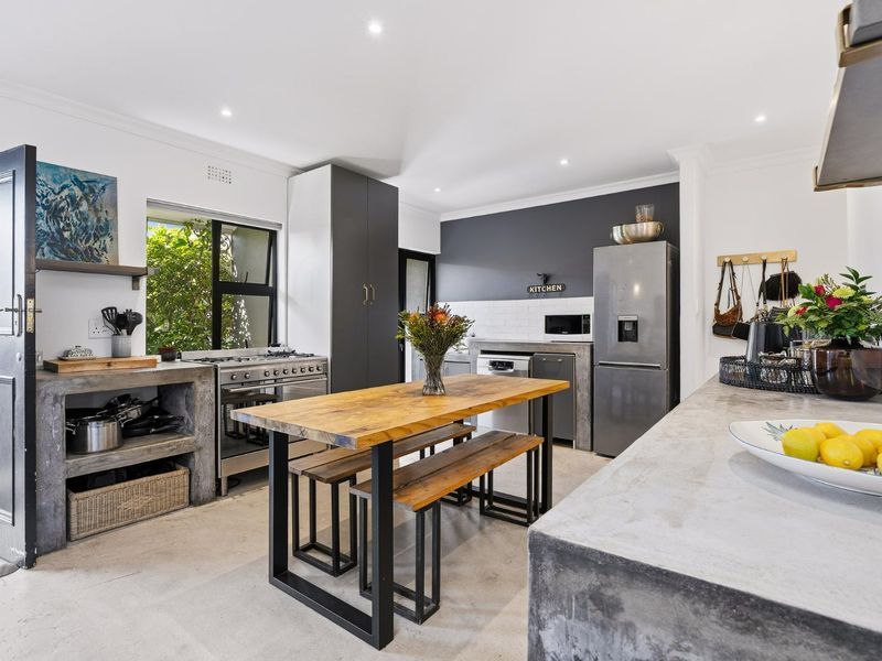 Modern kitchen featuring concrete countertops, subway tile backsplash, gas stove, and custom cabinetry with a central dining area.