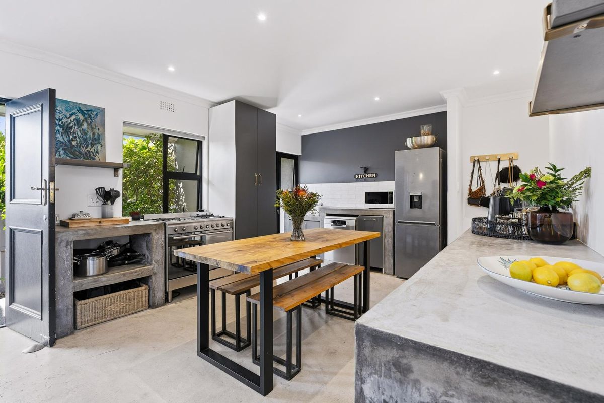 Modern kitchen featuring concrete countertops, subway tile backsplash, gas stove, and custom cabinetry with a central dining area.
