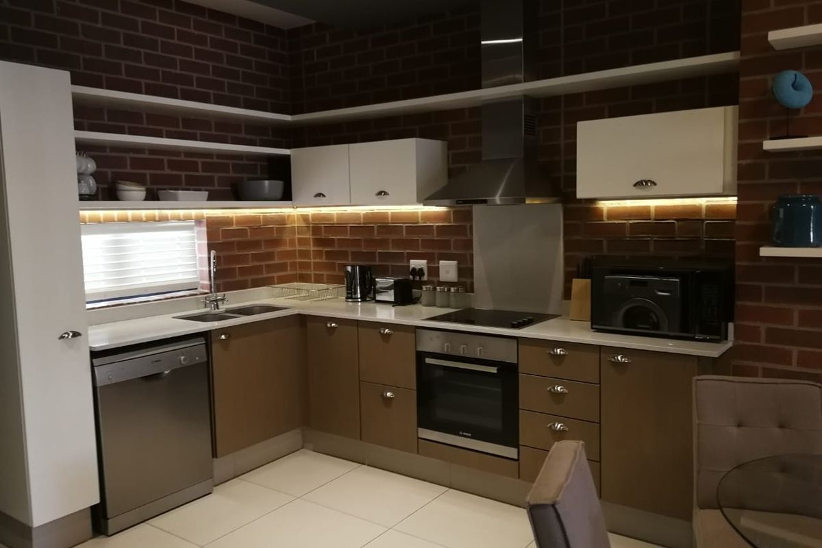 Modern kitchen featuring exposed brick walls, sleek cabinetry, stone countertops, integrated appliances, and stylish under-cabinet lighting.