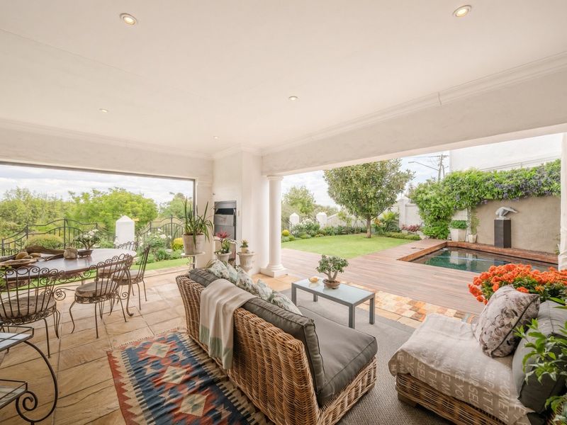 Spacious covered patio featuring stone flooring, recessed lighting, and a built-in fireplace, seamlessly flowing onto a timber deck with a swimming pool and garden.