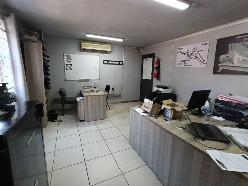 Functional industrial office space featuring tiled flooring, wall-mounted air conditioning, and overhead fluorescent lighting, suitable for administrative or operational use.