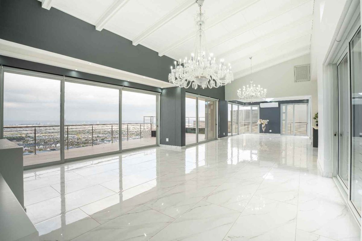 Spacious, light-filled living area featuring high vaulted ceilings, polished marble flooring, and expansive sliding glass doors opening to a panoramic balcony view.