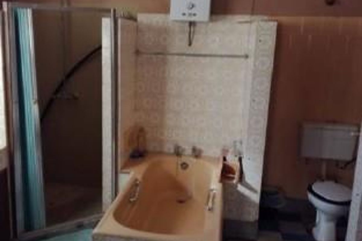 A dated bathroom featuring a built-in bathtub, a separate shower enclosure, a wall-mounted gas geyser, and a standard toilet.