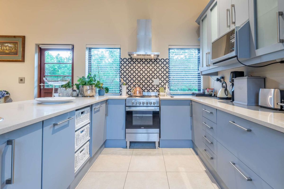 Modern kitchen featuring light blue cabinetry, stone countertops, a stainless steel gas stove with extractor fan, and a decorative tiled backsplash.