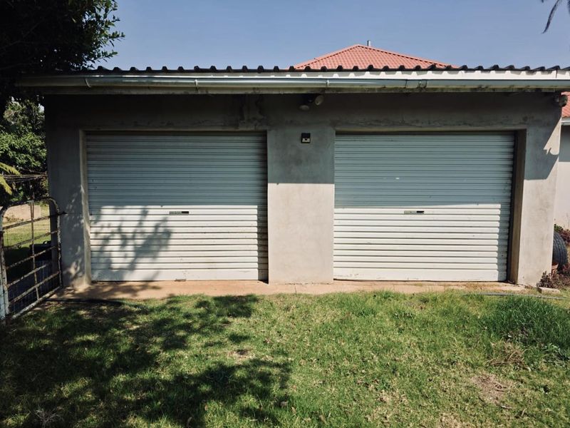A detached double garage featuring two white roller doors and a tiled roof, set against a grassed yard area.