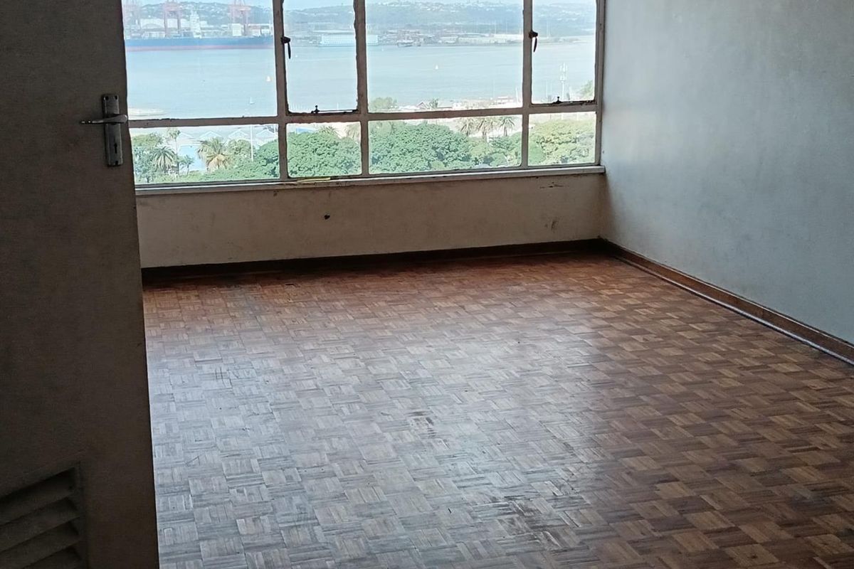 An empty bedroom featuring original parquet flooring and large windows offering expansive harbour and coastal views.