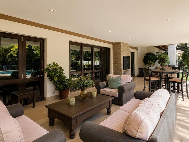 Spacious covered patio featuring tiled flooring, recessed lighting, and a built-in stone-clad fireplace, offering seamless access to the garden and pool area.