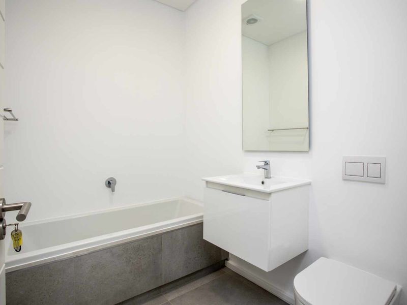 Modern bathroom featuring a wall-mounted vanity, built-in bathtub with grey tiling, wall-hung toilet with concealed cistern, and a sleek mirror.