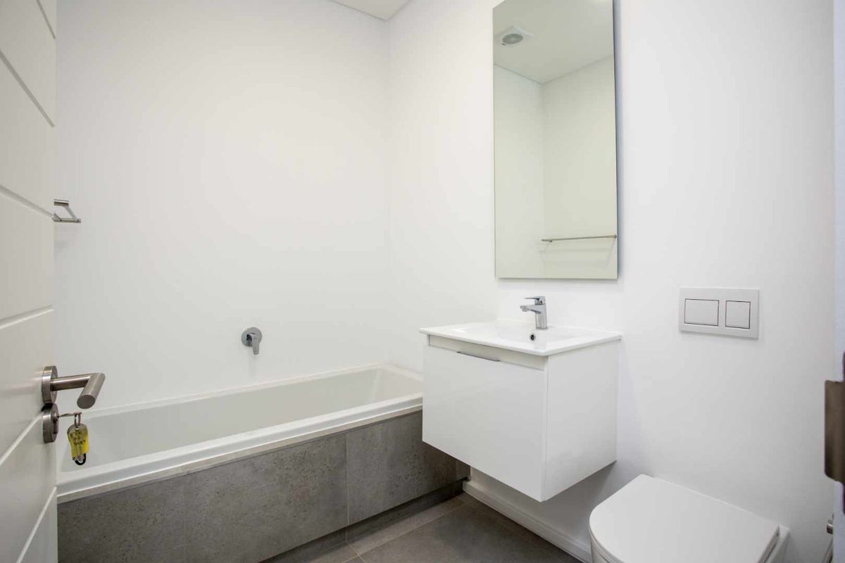 Modern bathroom featuring a wall-mounted vanity, built-in bathtub with grey tiling, wall-hung toilet with concealed cistern, and a sleek mirror.