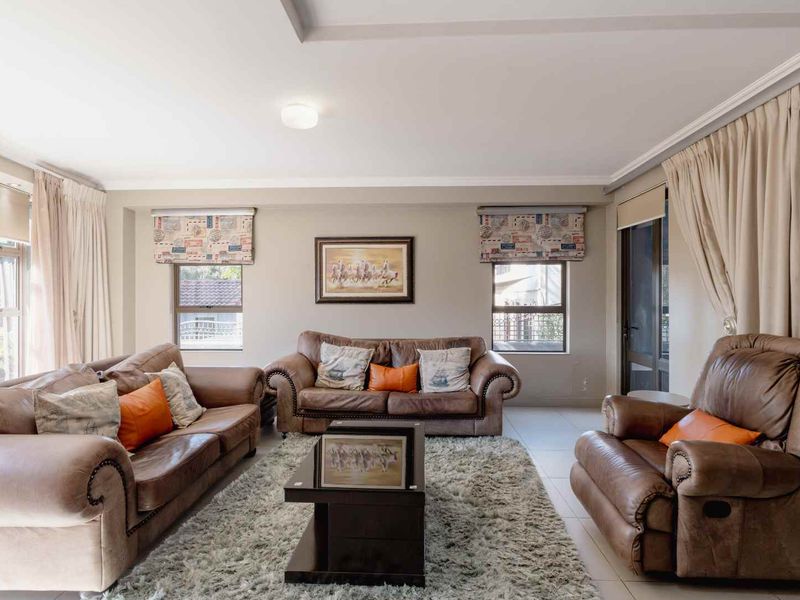 A spacious living room featuring neutral tiled flooring, recessed ceiling detailing, and large windows that provide ample natural light.