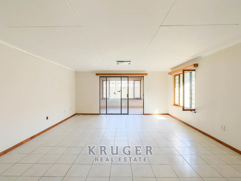 A spacious, empty living area featuring neutral tiled flooring, large windows, and a sliding glass door leading to an outdoor space.