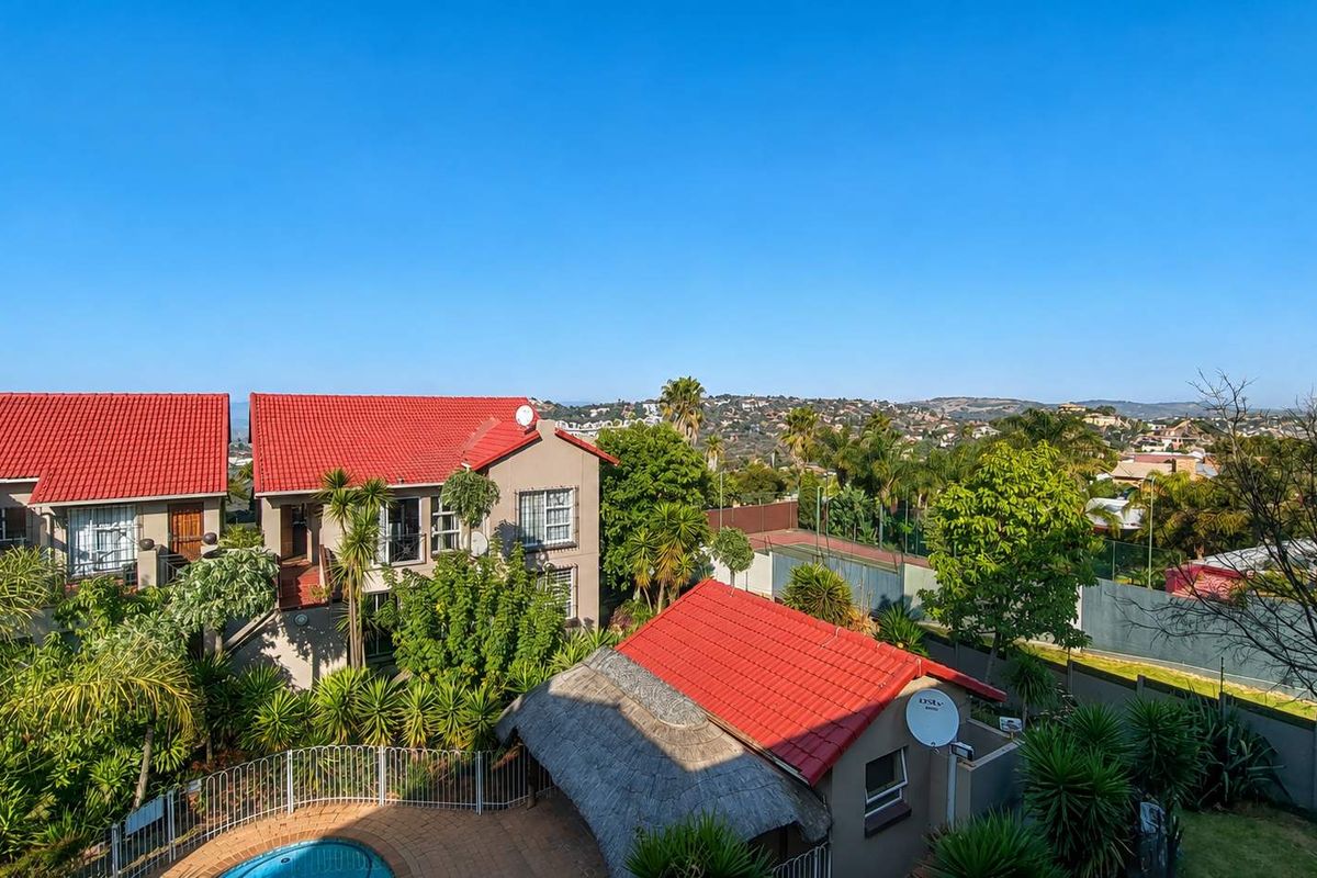 Aerial view of a townhouse complex featuring a swimming pool, a thatched lapa, and well-maintained garden areas with scenic neighborhood views.