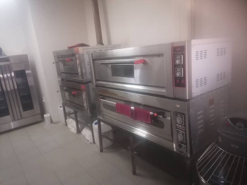 A commercial kitchen space featuring multiple stacked stainless steel deck ovens and tiled flooring, suitable for professional food preparation.