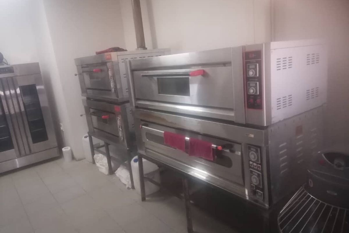 A commercial kitchen space featuring multiple stacked stainless steel deck ovens and tiled flooring, suitable for professional food preparation.